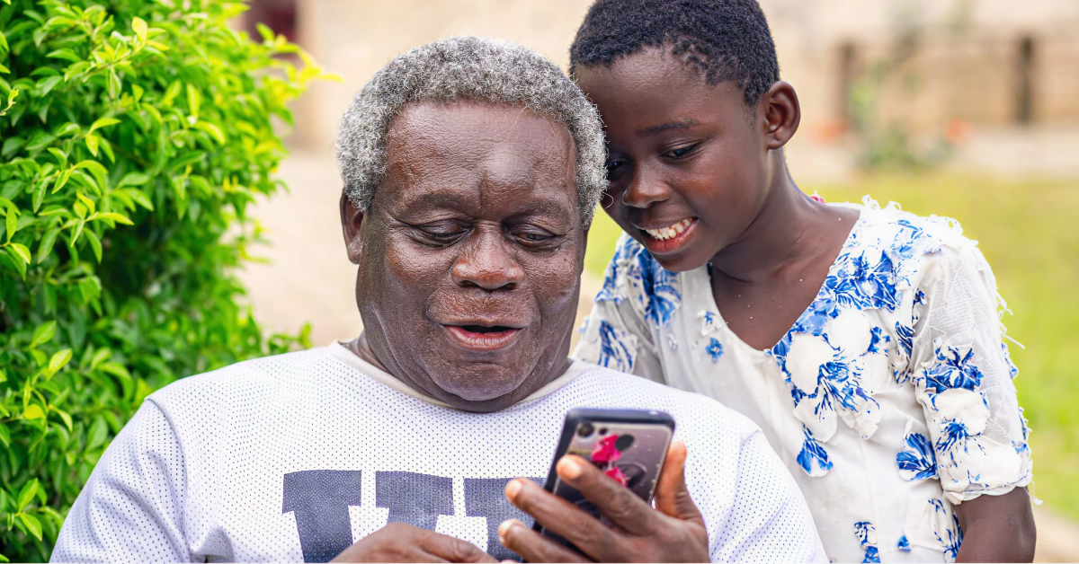 A Ghanaian grandfather and grandchild looking at a phone together.